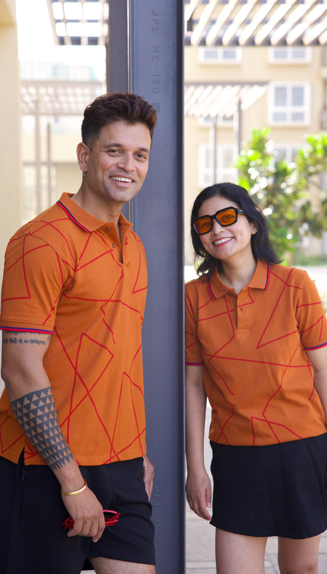 Two people wearing matching orange polo shirts with geometric patterns outdoors.