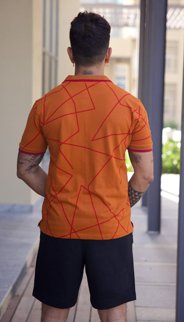 Person wearing an orange shirt with red geometric patterns and black shorts, standing in a modern outdoor setting.