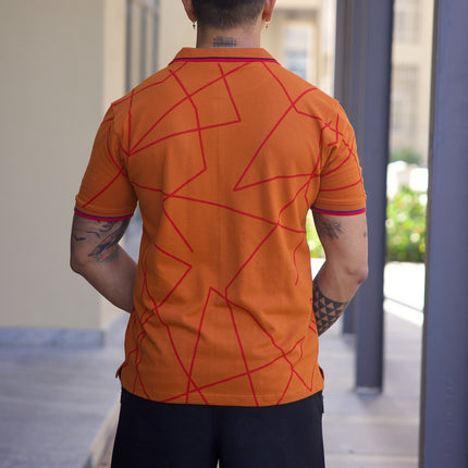 Person wearing an orange shirt with red geometric patterns and black shorts, standing in a modern outdoor setting.