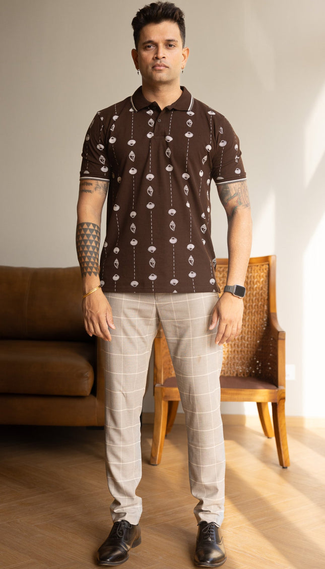 Man wearing a patterned shirt and light pants standing in a room with a couch and chair.