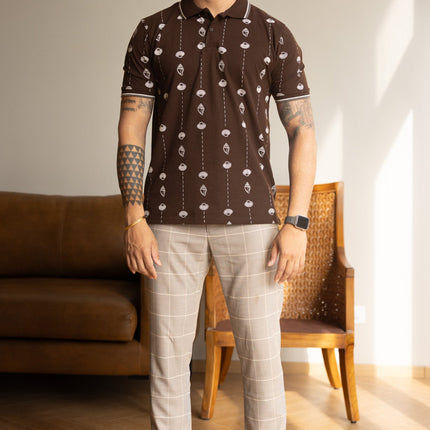 Man wearing a patterned shirt and light pants standing in a room with a couch and chair.
