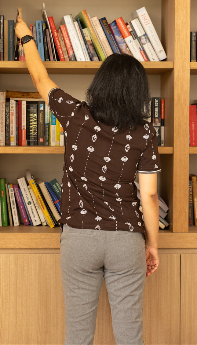 Person reaching for a book on a tall wooden bookshelf filled with books.