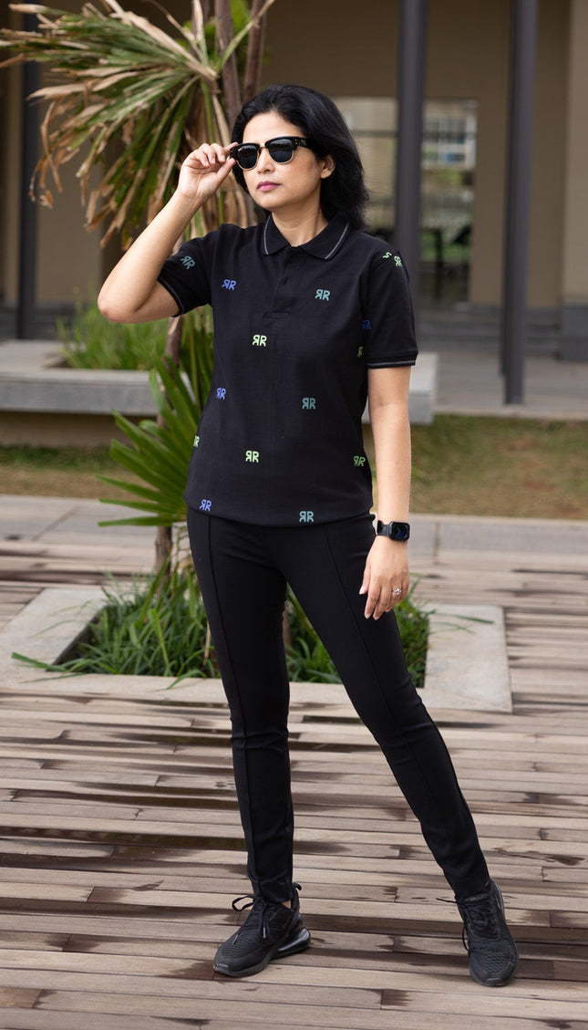 Person wearing a black outfit with sunglasses outdoors on a wooden deck.