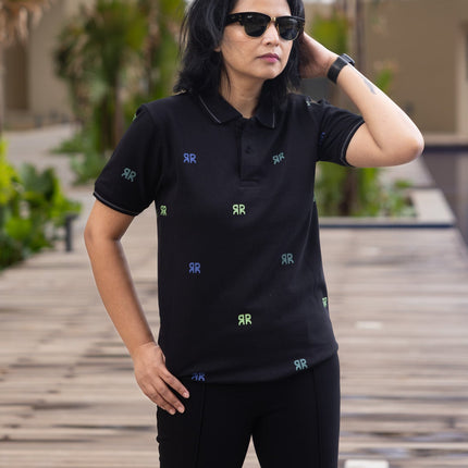 Person wearing a black polo shirt with small patterns, standing on a wooden deck with buildings in the background.