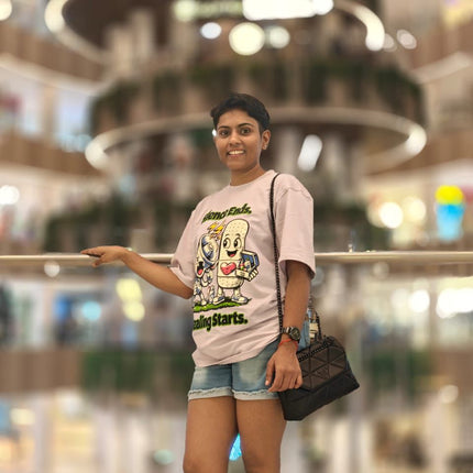 Woman in a RREFLEKT pink t-shirt with cartoon characters and denim shorts standing in a modern indoor setting.