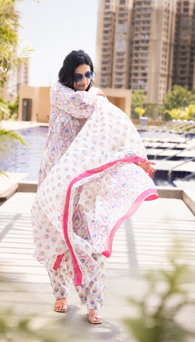 Woman in a floral dress with pink trim standing by a poolside with buildings in the background