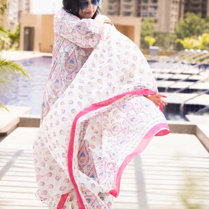 Woman in a floral dress with pink trim standing by a poolside with buildings in the background