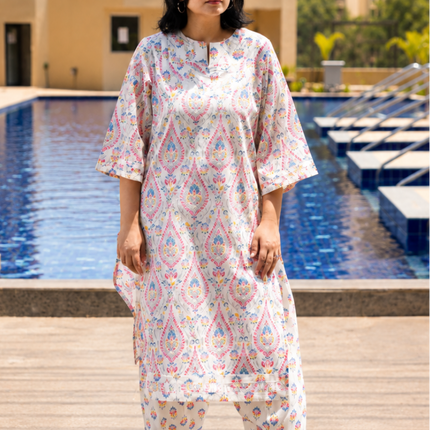 Woman in a white patterned outfit standing by a pool with buildings in the background