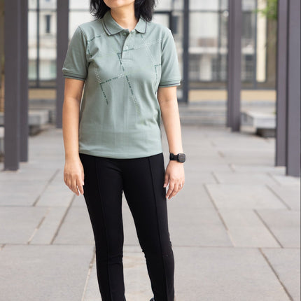 Woman wearing a green polo shirt and black pants standing in an outdoor setting.
