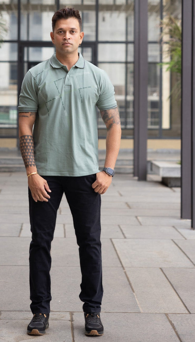 Man wearing a green polo shirt and dark pants standing under a wooden canopy.
