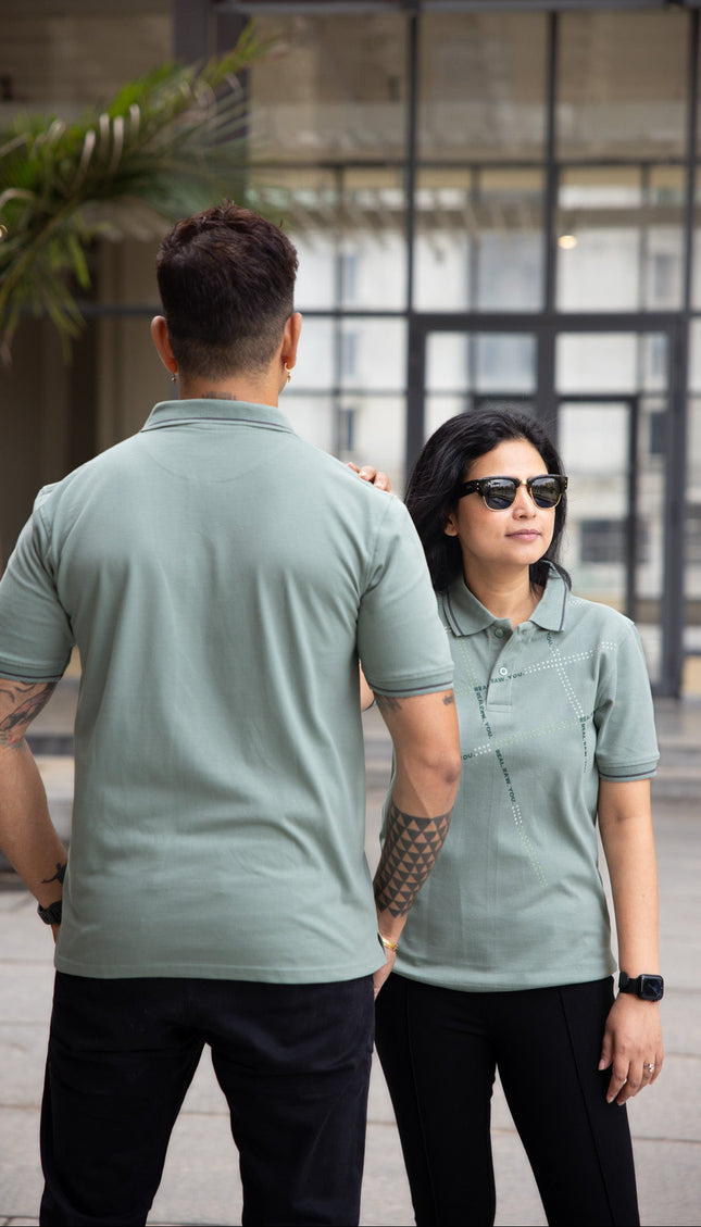 Two people wearing matching green polo shirts outdoors.