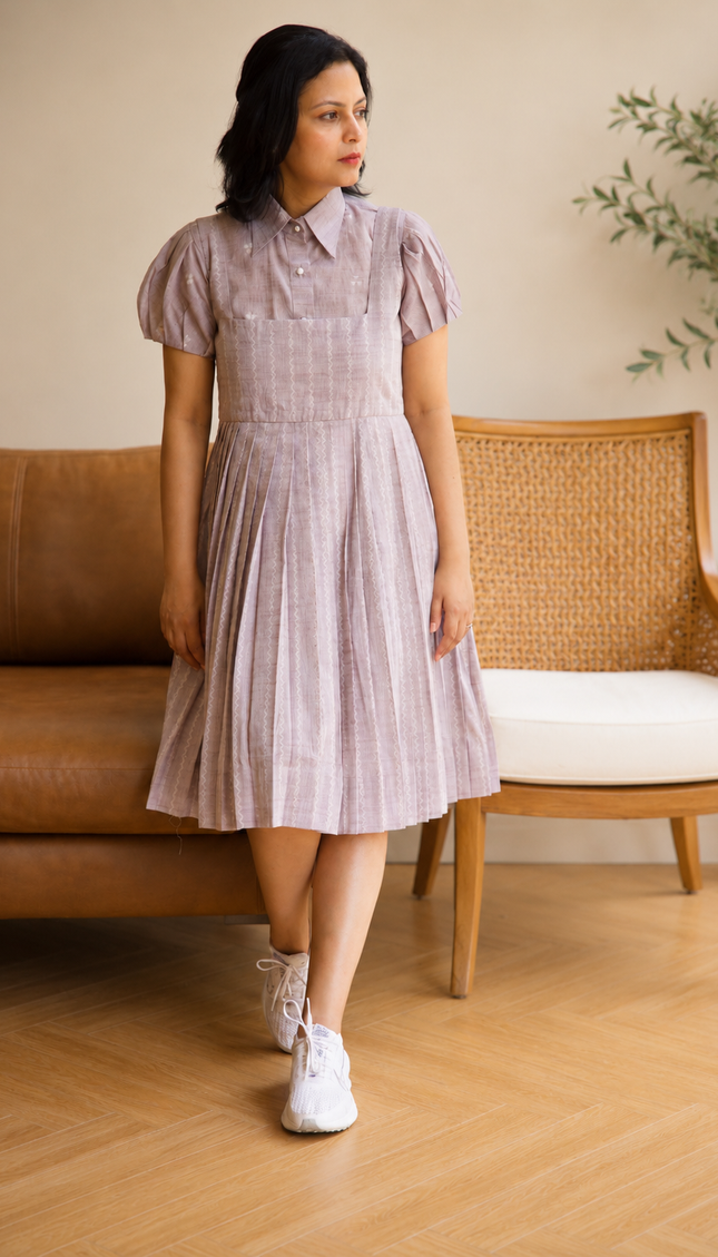 Woman wearing a checkered dress standing in a room with a couch and plant.