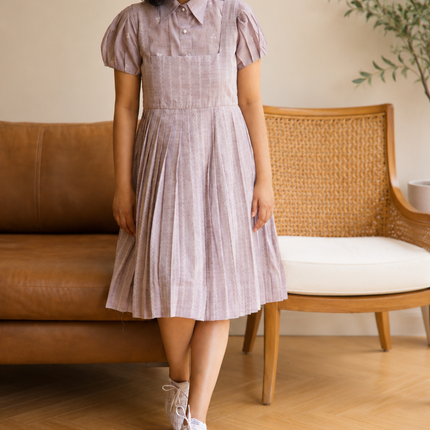 Woman wearing a checkered dress standing in a room with a couch and plant.