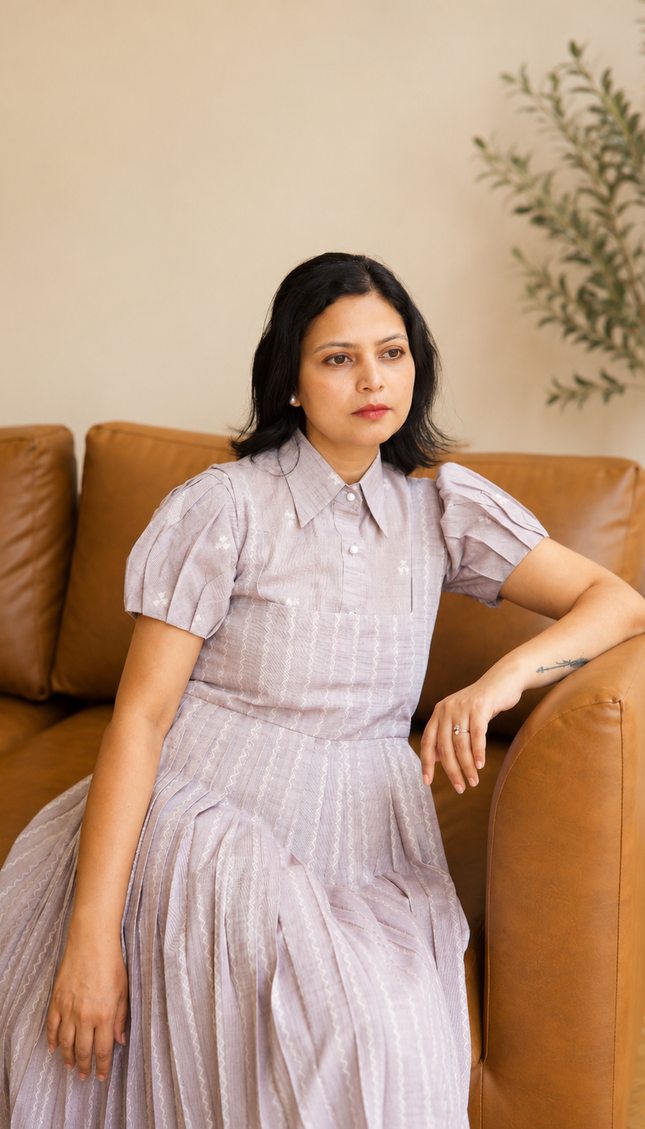 Woman in a light grey dress sitting on a brown leather couch with a plant in the background.