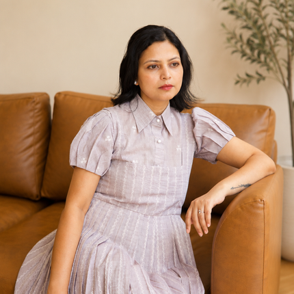 Woman in a light grey dress sitting on a brown leather couch with a plant in the background.