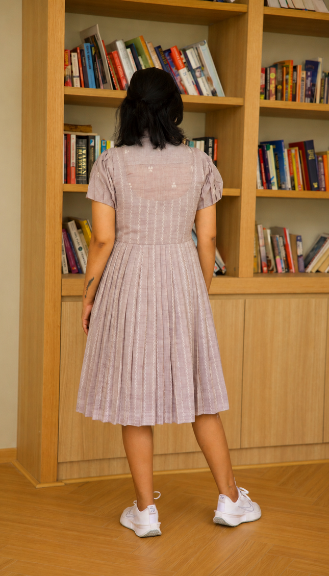 Person wearing a dress standing in front of a bookshelf filled with books.
