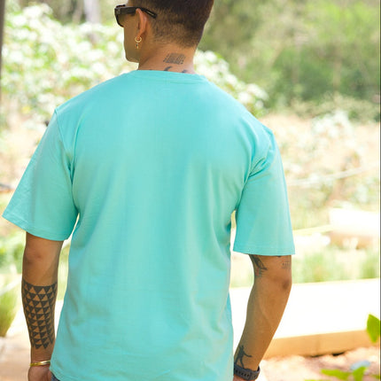 Person wearing a light blue shirt and sunglasses, standing in a forested area.