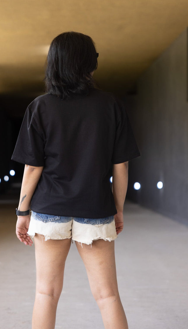 Person wearing a black shirt and white shorts standing in a tunnel-like structure with a light fixture on the wall.
