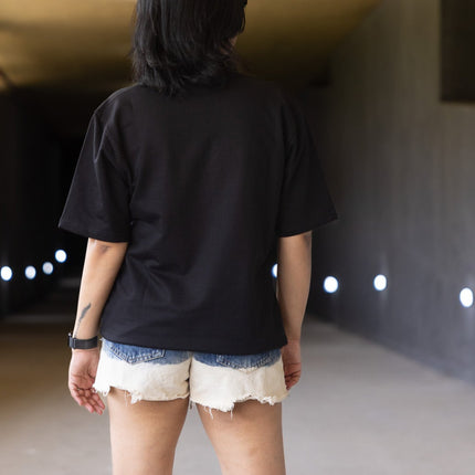 Person wearing a black shirt and white shorts standing in a tunnel-like structure with a light fixture on the wall.