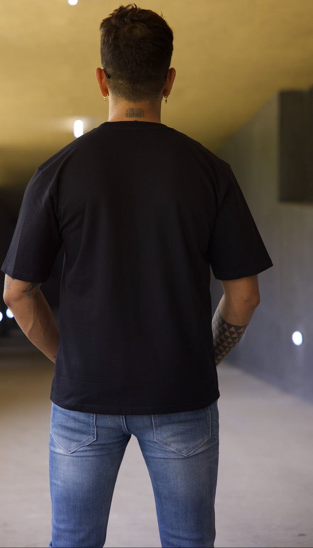 Man wearing a black t-shirt and blue jeans walking away in a tunnel.