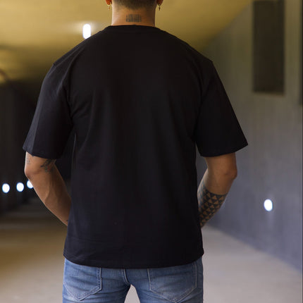 Man wearing a black t-shirt and blue jeans walking away in a tunnel.