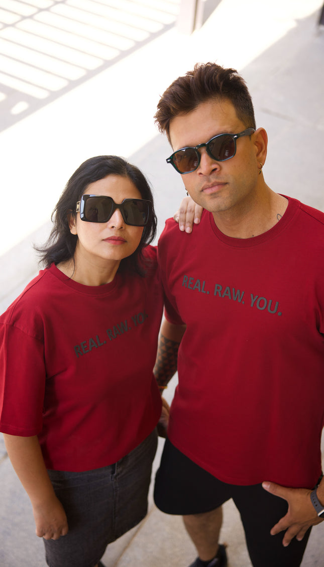 Two people wearing red t-shirts with text, standing close together indoors.