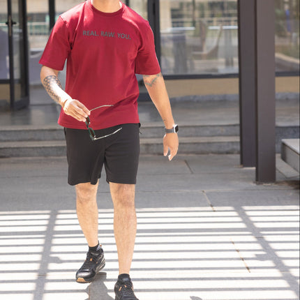 Man in red shirt and black shorts walking on a crosswalk with a blurred background