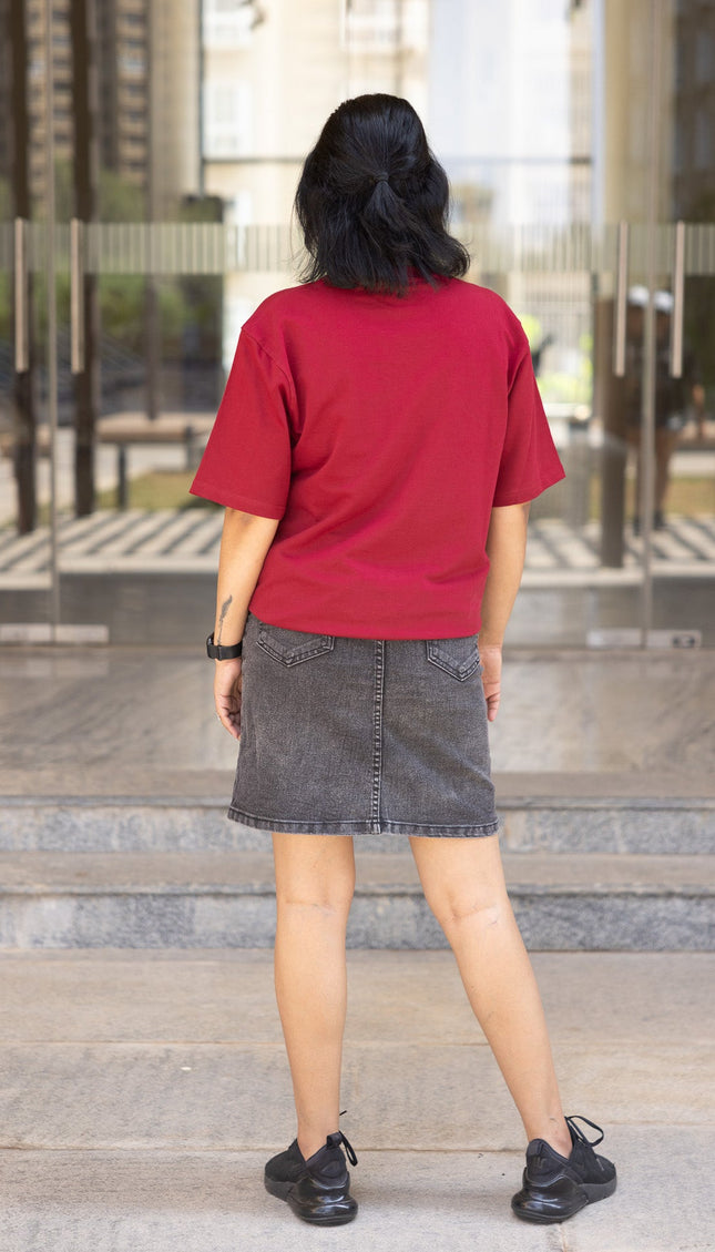 Person wearing a red shirt and black skirt standing in front of a glass building.