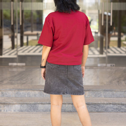 Person wearing a red shirt and black skirt standing in front of a glass building.