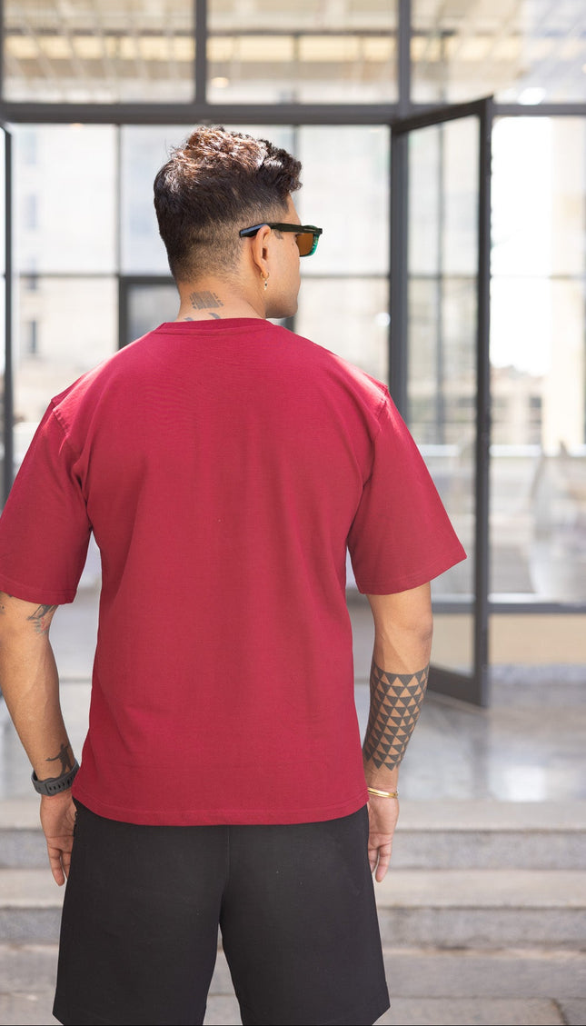 Man wearing a red shirt and black shorts standing in front of a modern building entrance.