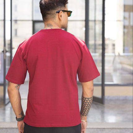 Man wearing a red shirt and black shorts standing in front of a modern building entrance.