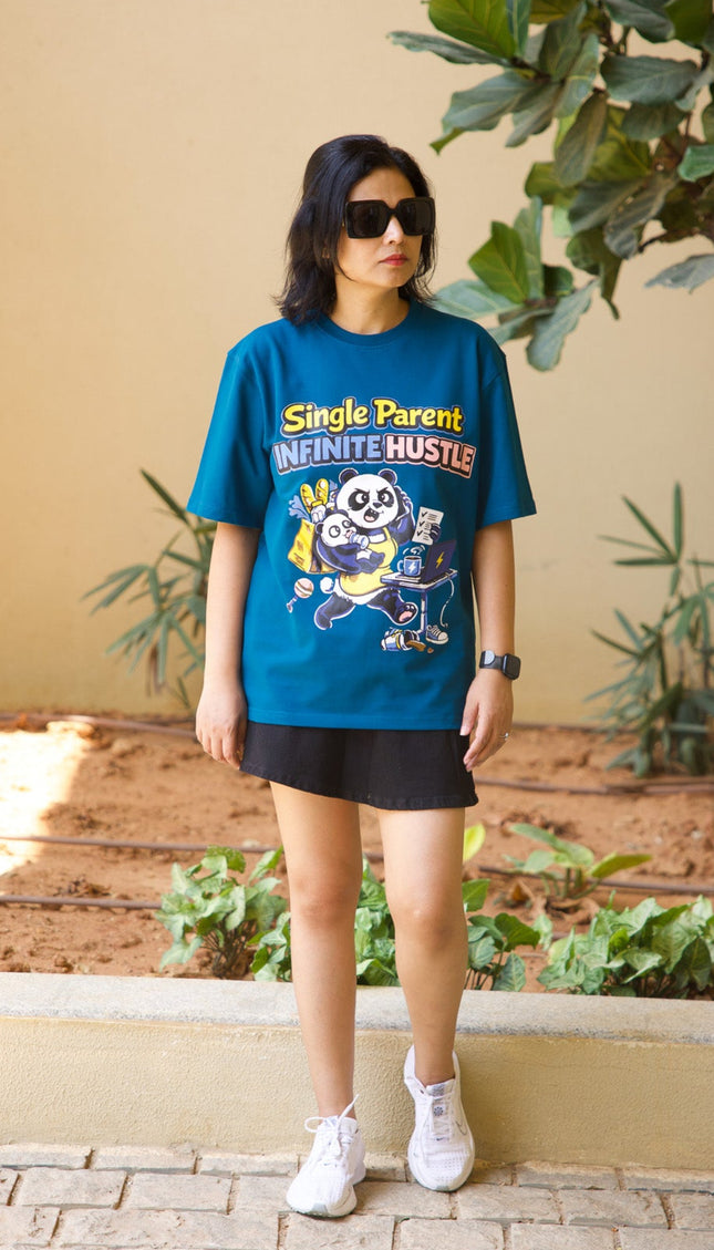 Person wearing a blue graphic t-shirt with text and graphics, standing outdoors with plants in the background.