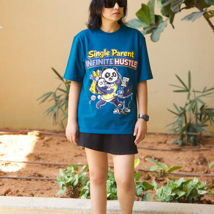 Person wearing a blue graphic t-shirt with text and graphics, standing outdoors with plants in the background.