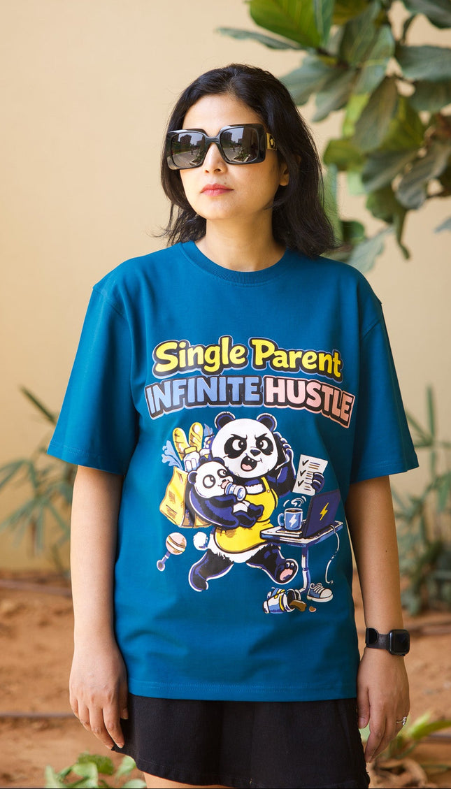Person wearing a blue t-shirt with graphic design and text, standing indoors with plants in the background.