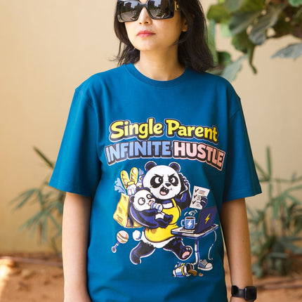 Person wearing a blue t-shirt with graphic design and text, standing indoors with plants in the background.