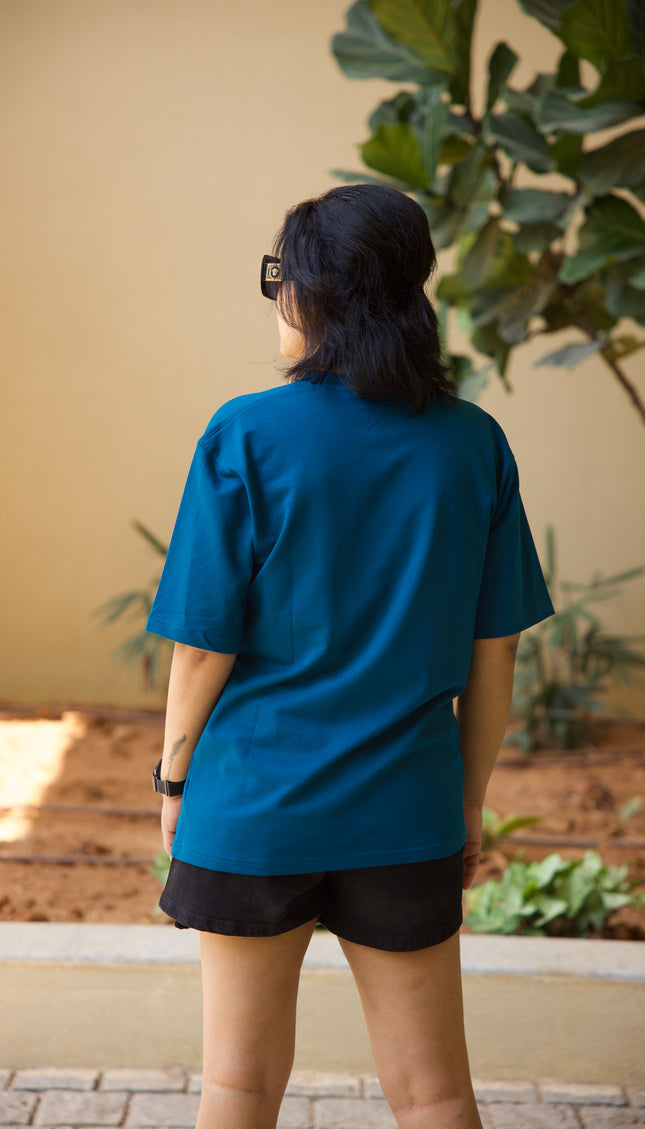 Person wearing a blue shirt and black shorts standing outdoors with plants in the background