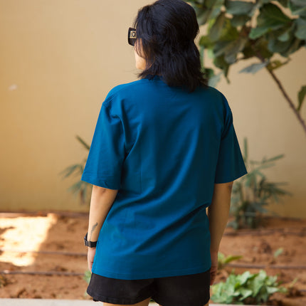 Person wearing a blue shirt and black shorts standing outdoors with plants in the background