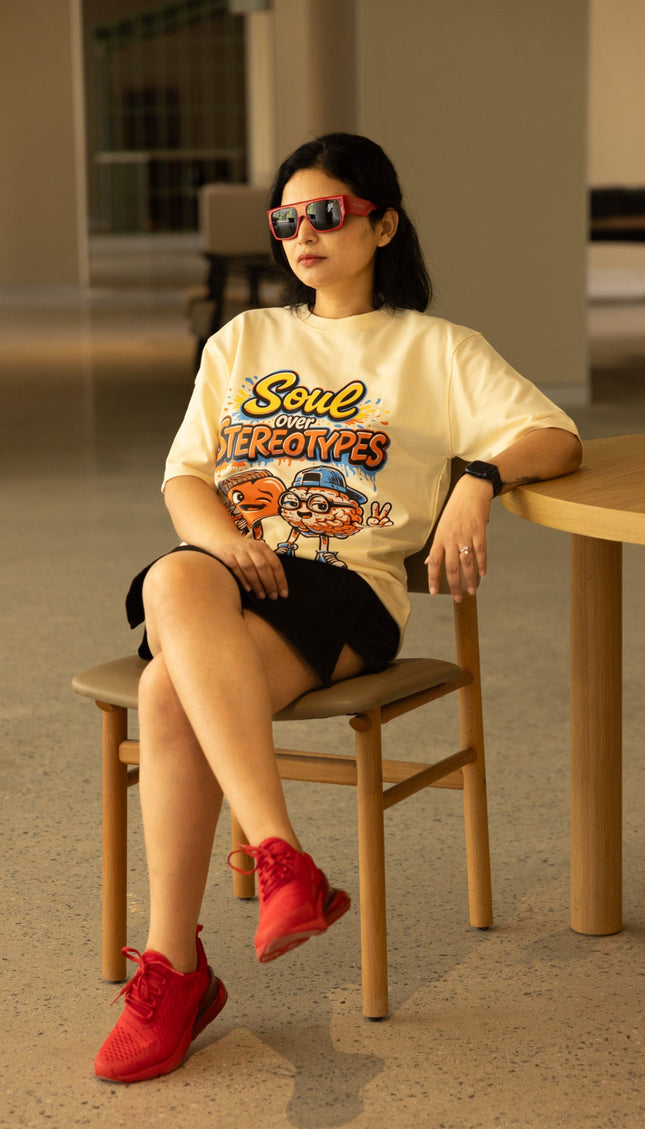 Woman sitting on a chair wearing a graphic t-shirt and red shoes in an indoor setting.