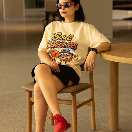 Woman sitting on a chair wearing a graphic t-shirt and red shoes in an indoor setting.