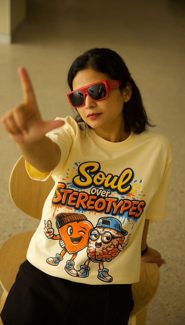 Person wearing a yellow t-shirt with 'Soul over Stereotypes' design, sitting on a chair.