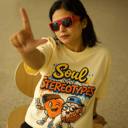 Person wearing a yellow t-shirt with 'Soul over Stereotypes' design, sitting on a chair.