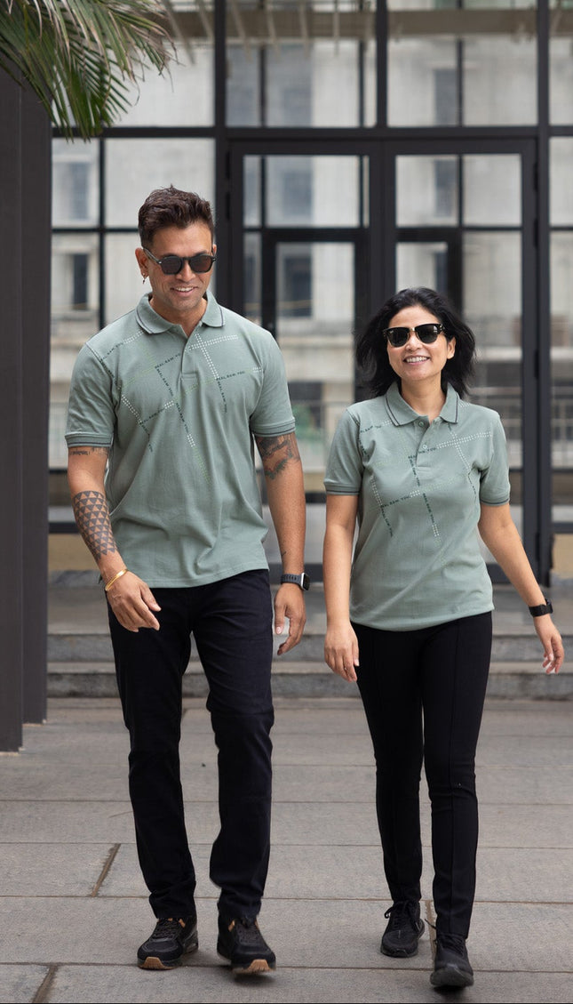 Two people wearing matching green shirts and black pants walking outdoors.